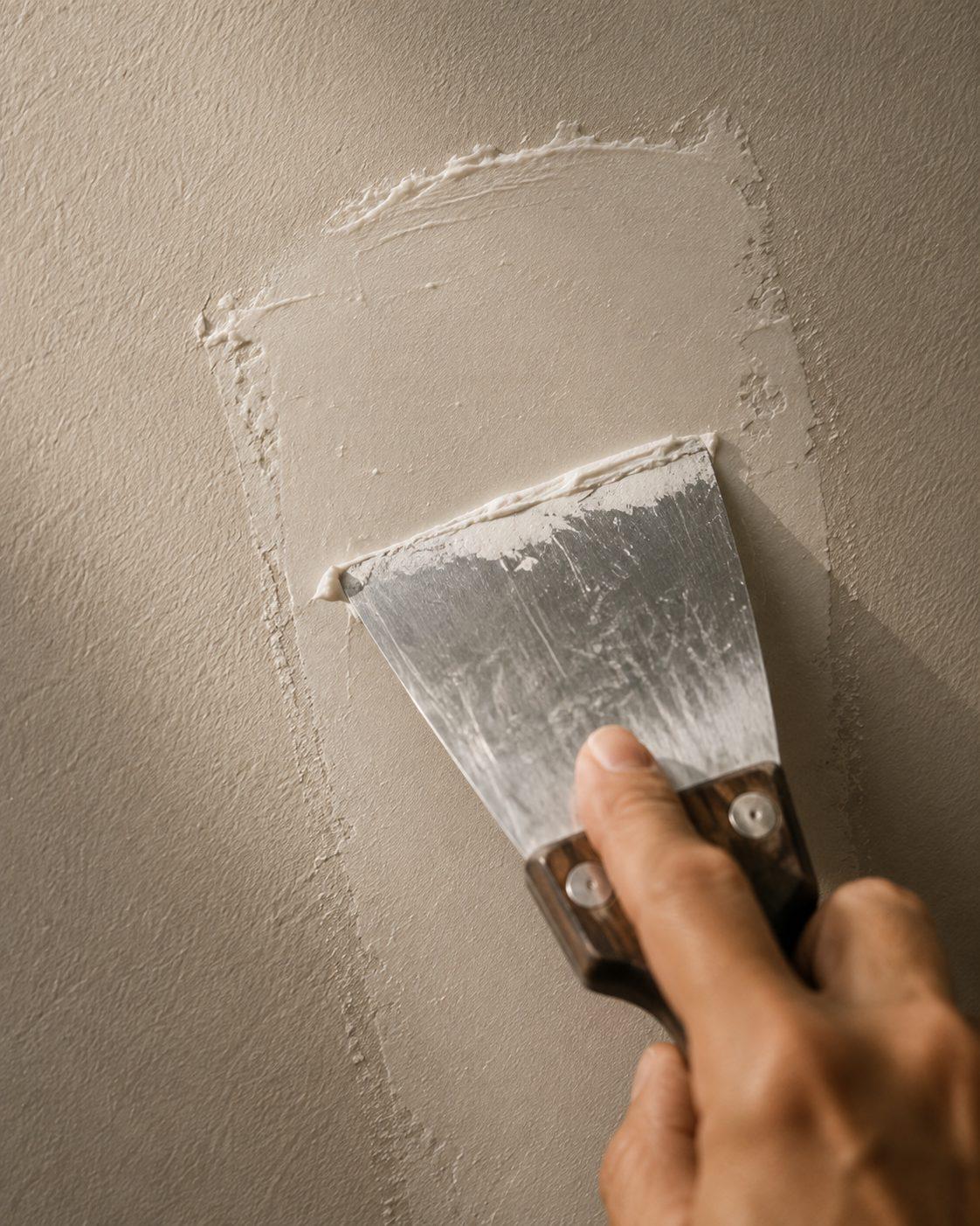 A taping knife spreading compound across a drywall patch