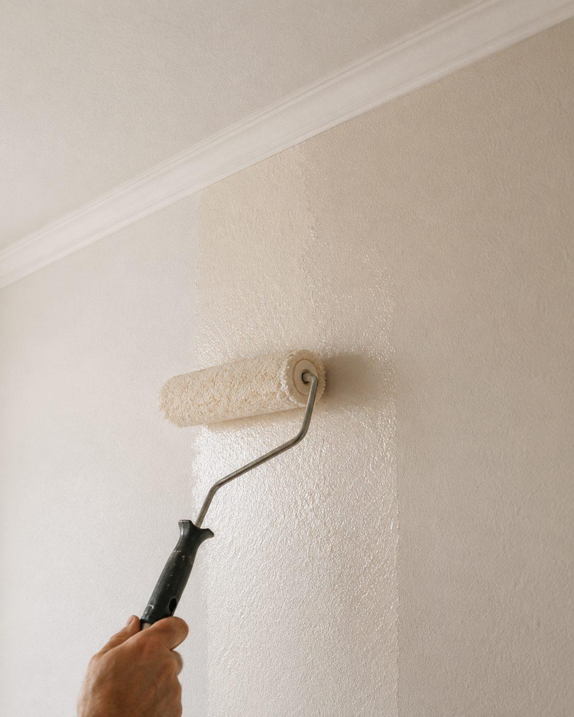 A roller applying a clean coat of paint to an interior wall below cornice